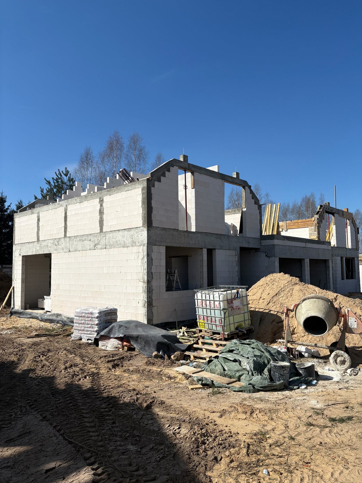 Modern house under construction with concrete block walls, open window frames, and construction materials scattered in front yard