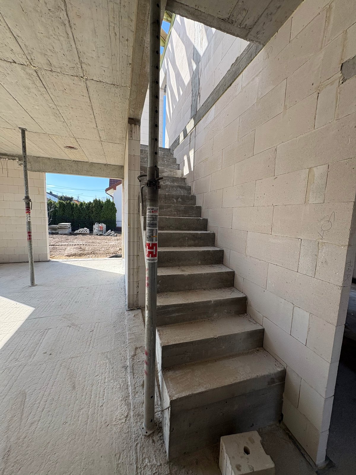 Concrete staircase in unfinished building interior with cinder block walls and view to outdoor area