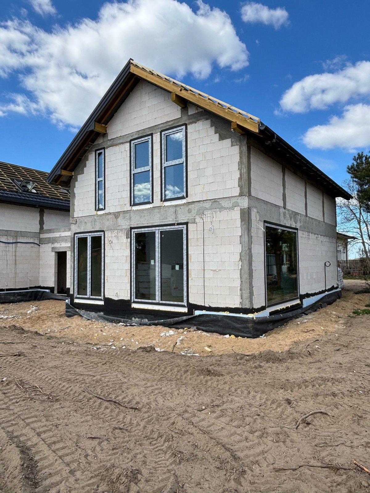 New two-story white house under construction with black trim and large windows on bare dirt lot