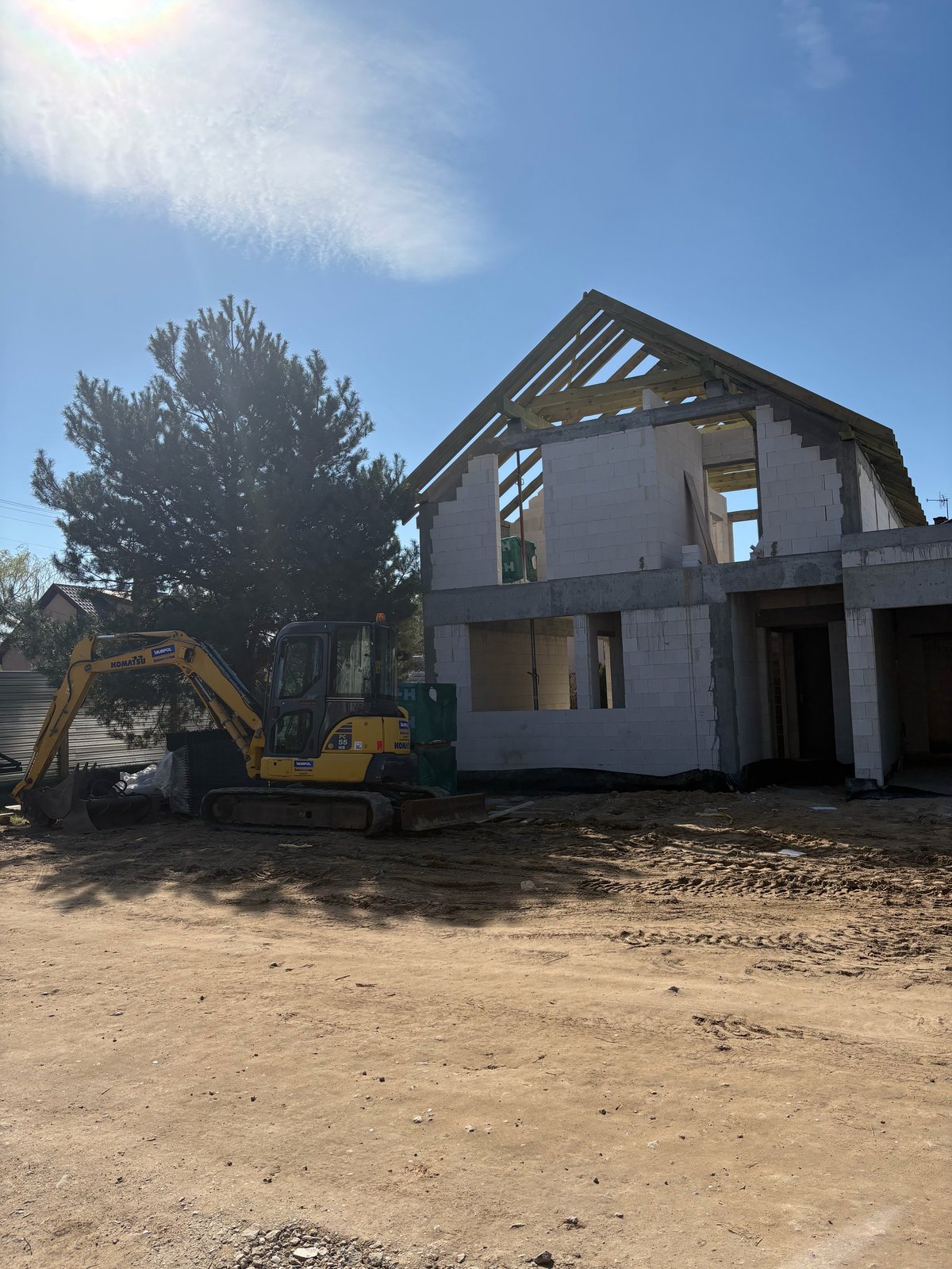 Construction site with yellow excavator and modern house frame under construction on dirt ground
