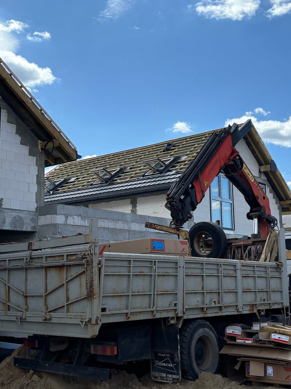 Truck with red hydraulic crane unloading materials at a residential building under construction with white siding